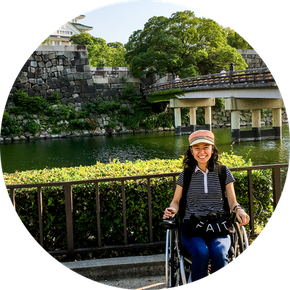 Smiling student  in wheelchair with river and bridge in background.