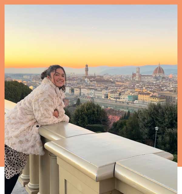 Student leans on stone balcony wall overlooking Florence at sunset.
